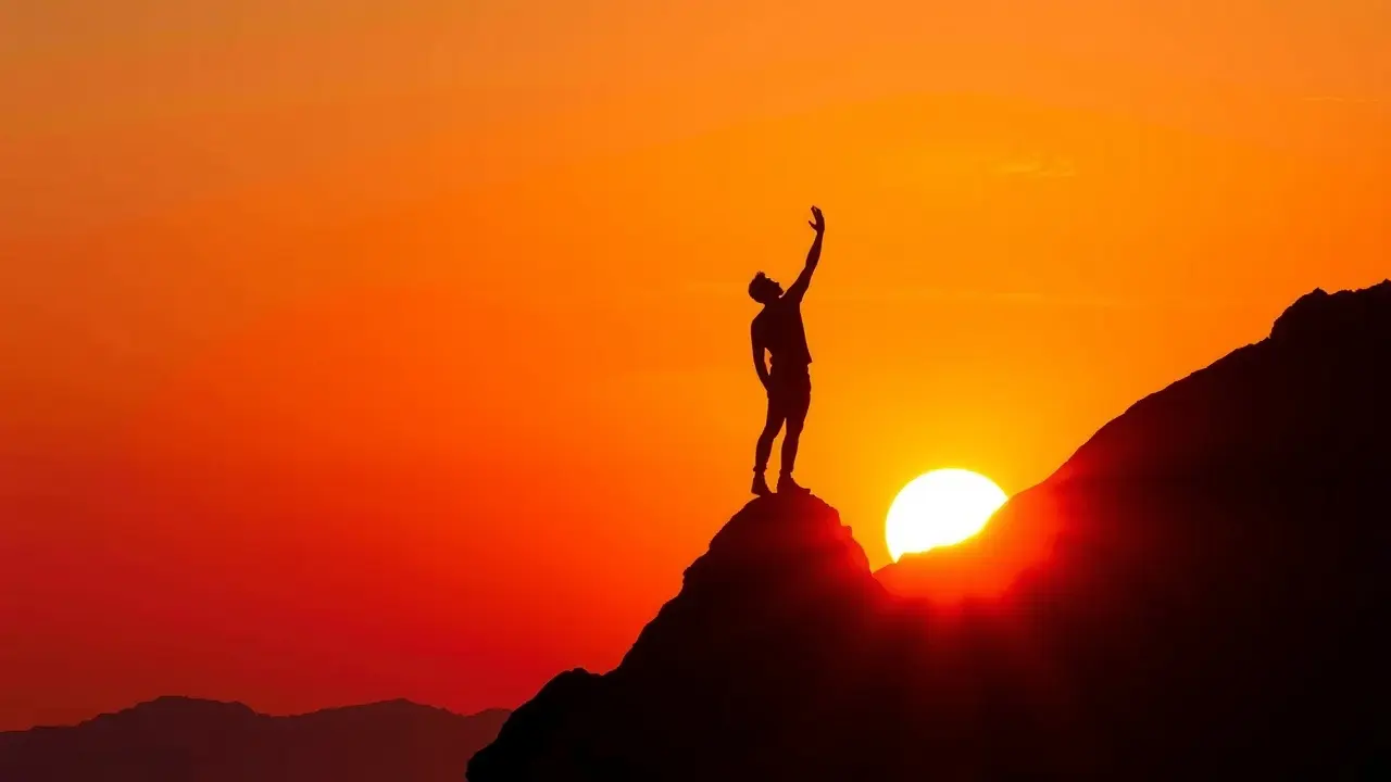 Pessoa no topo da montanha ao pôr do sol, meta alcançada.